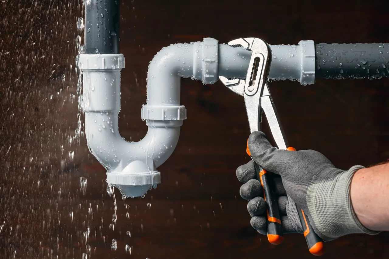 Gloved hand repairing a leaking drain pipe